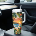 A colorful insulated tumbler with a tropical beach scene printed on it, sitting on the passenger seat of a car.